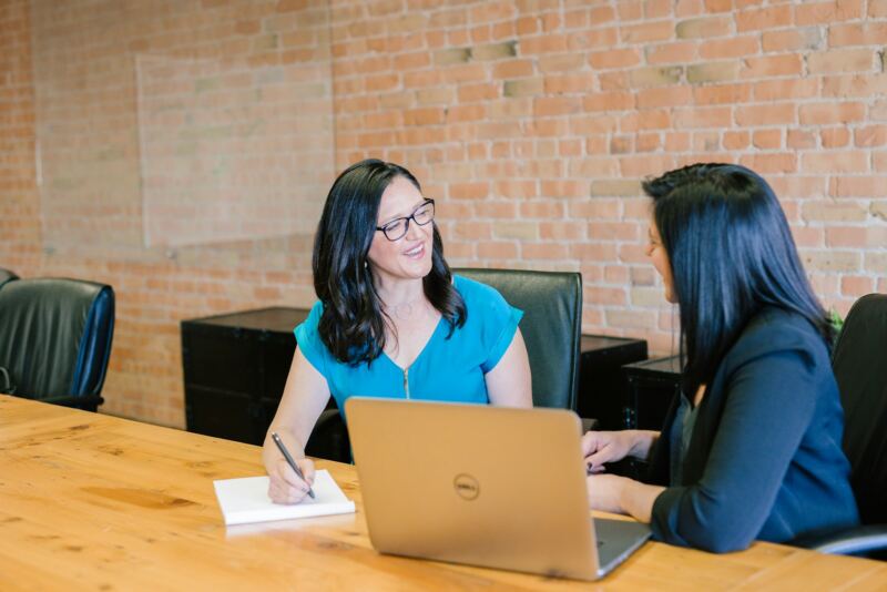 Two colleagues talking one on one at a table with a laptop
