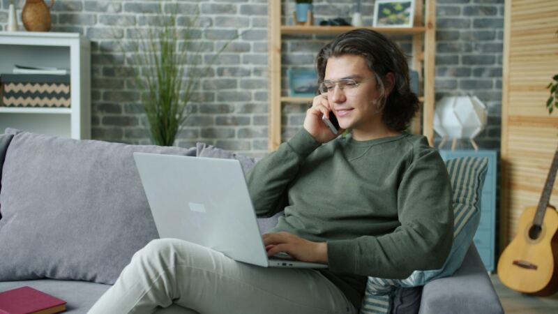 A man on the phone with his laptop open on the couch