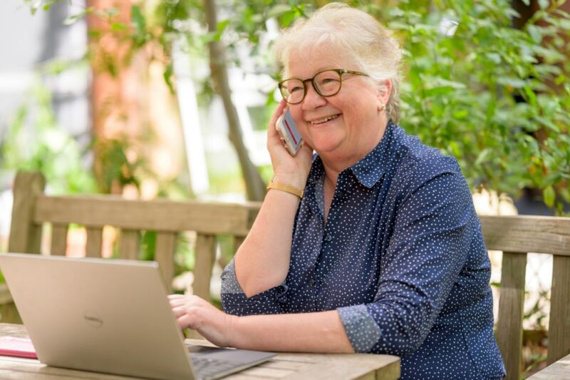 An older woman smiling while she talks on the phone at her laptop