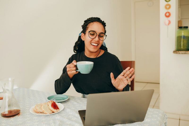 A woman with a cup of tea on a video call at her table